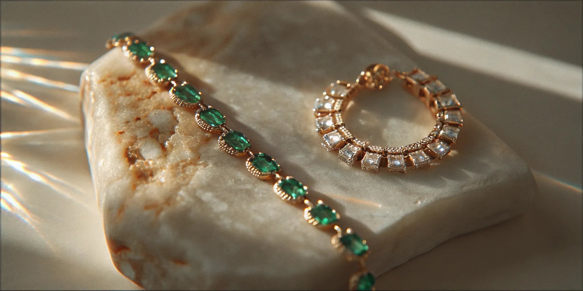 Emerald and diamond fine jewelry arranged on ivory stone