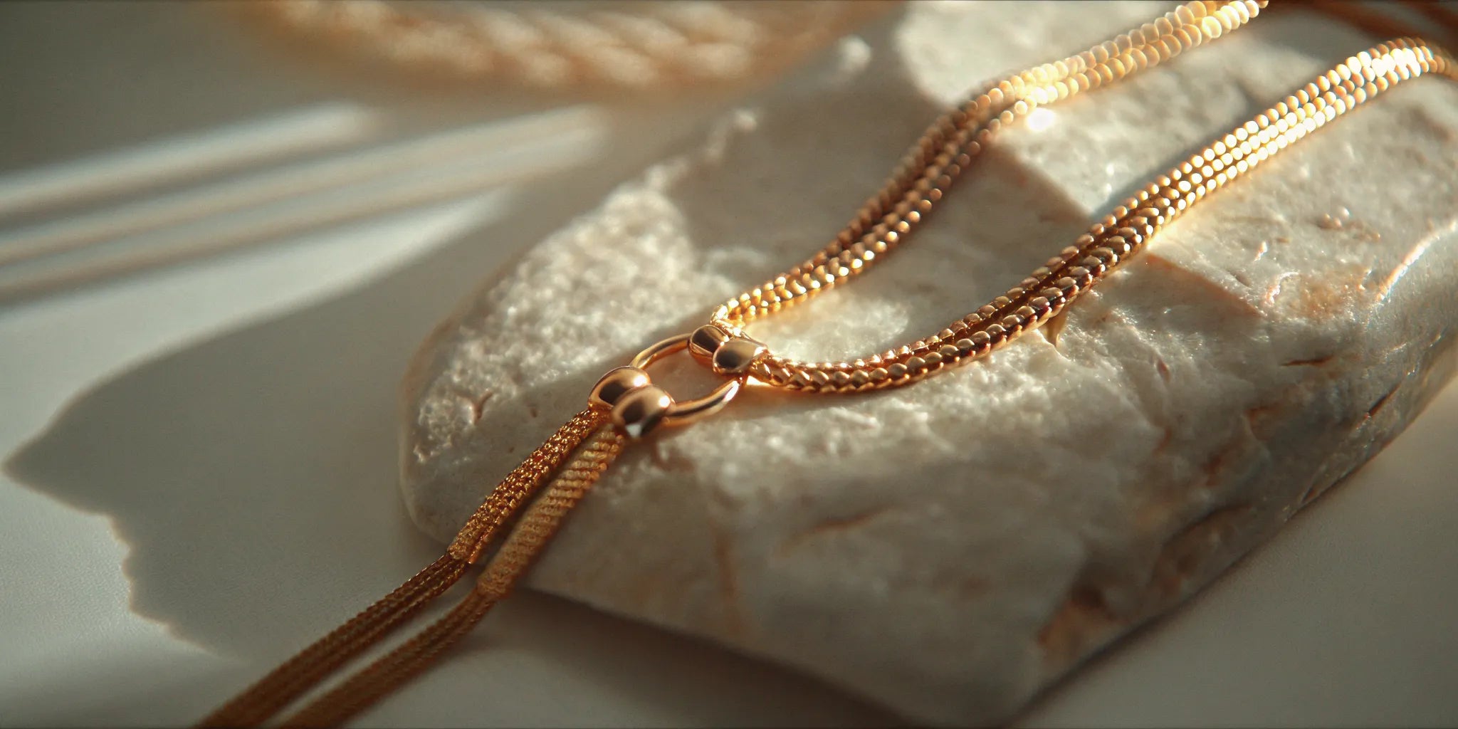 Yellow gold lariat necklace arranged on warm cream stone
