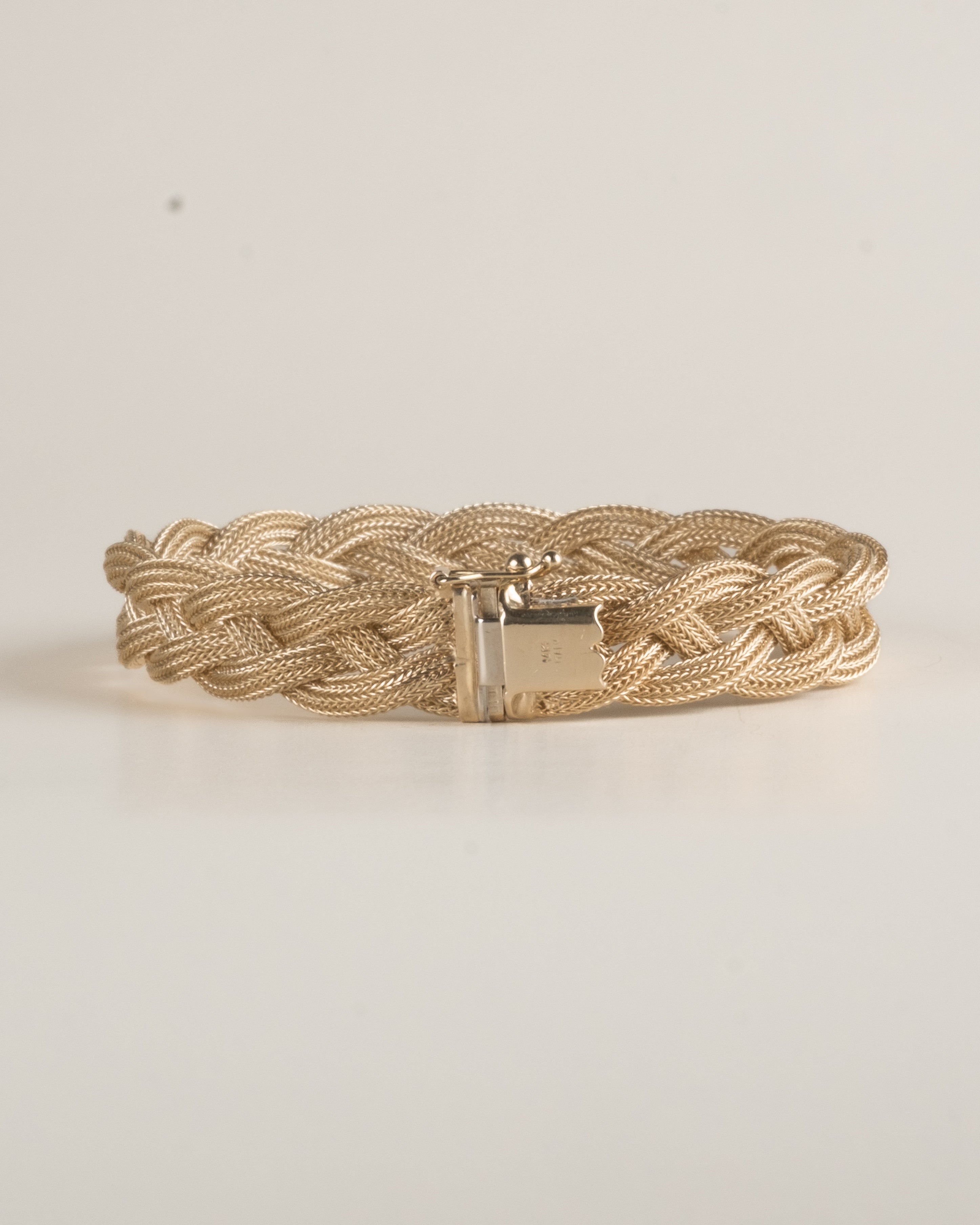 Gold braided bracelet on a light beige background