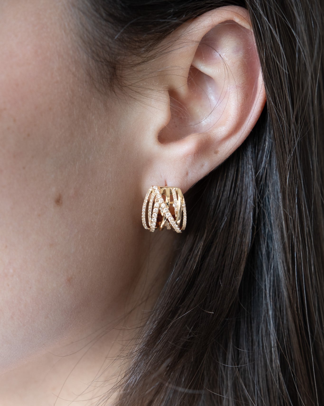 Close-up of a person wearing gold hoop earrings with dark hair.