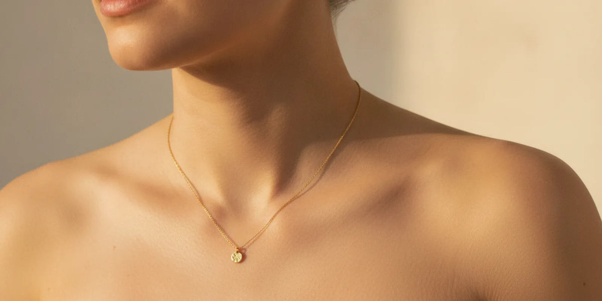 Close-up of a person wearing simple gold earrings and a necklace against bare skin