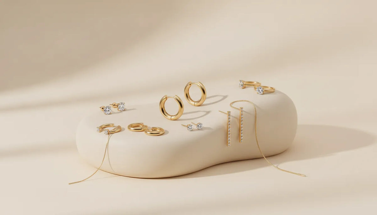 Gold stud, hoop, huggie, drop, and threader earrings arranged on an ivory display