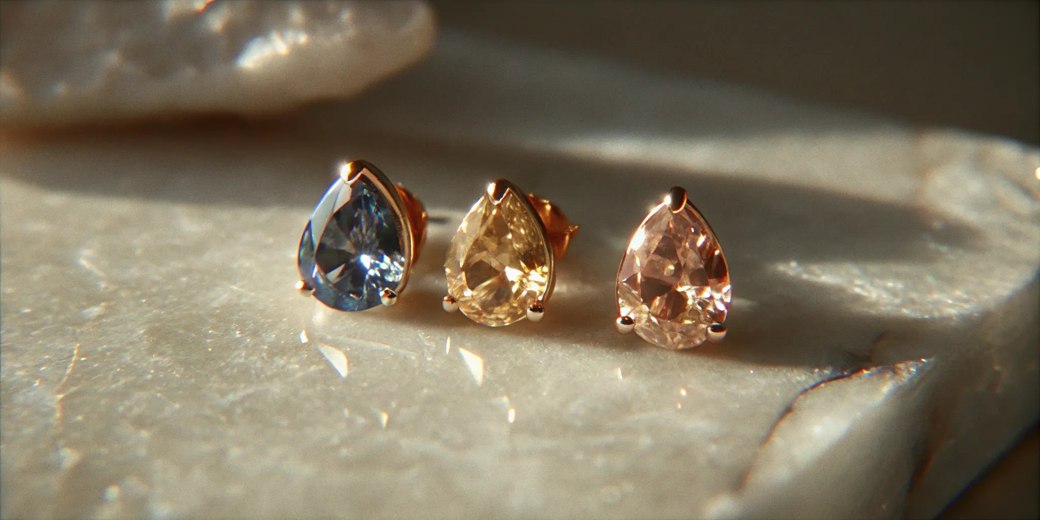 Gold pear shaped stud earrings with blue, yellow, and pink gemstones.