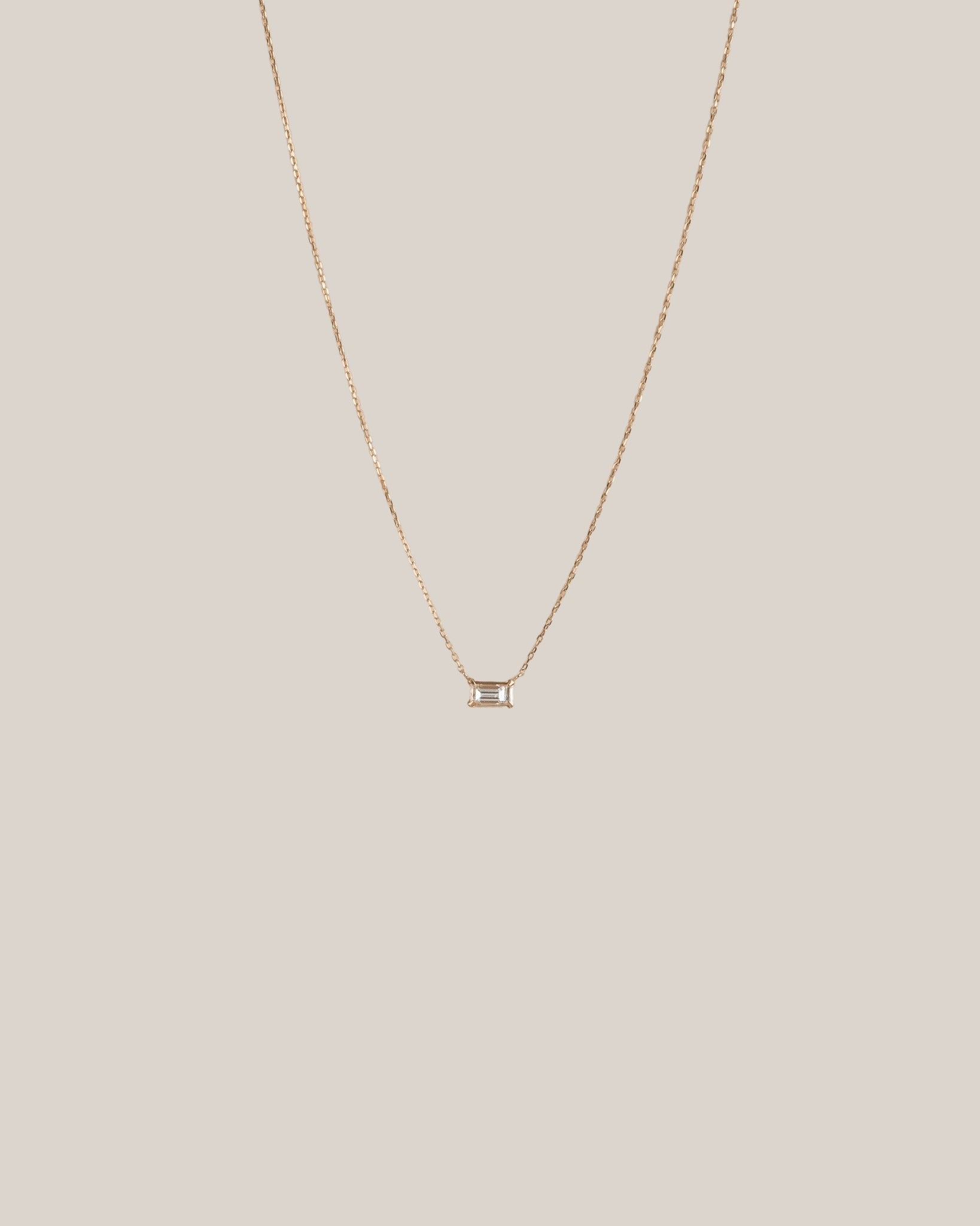 Gold necklace with a small pendant on a beige background