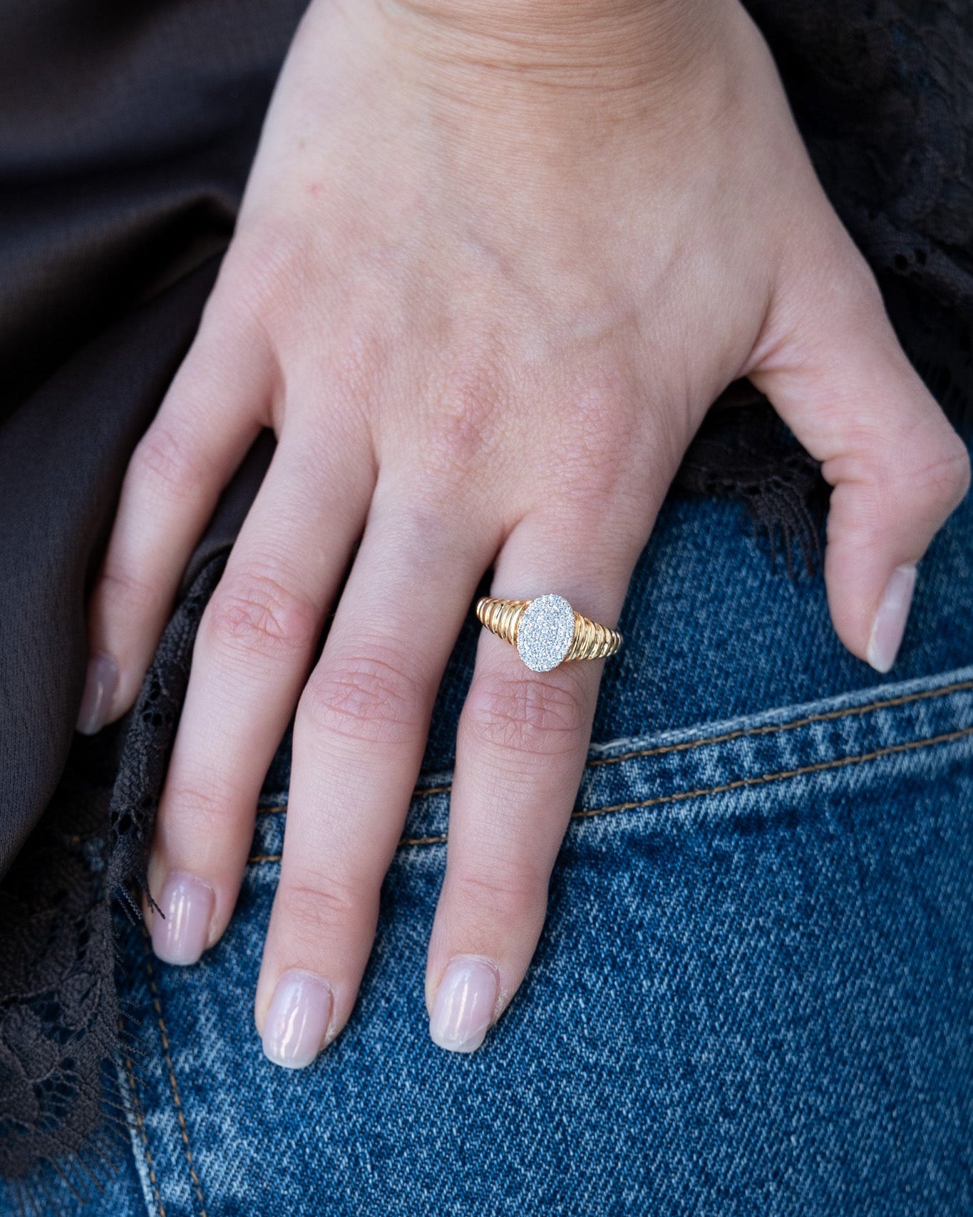 Hand wearing a gold ring with a diamond on a denim background