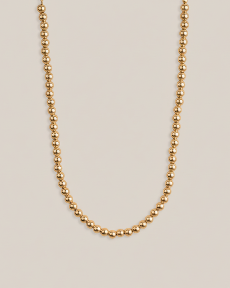 Gold beaded necklace on a beige background