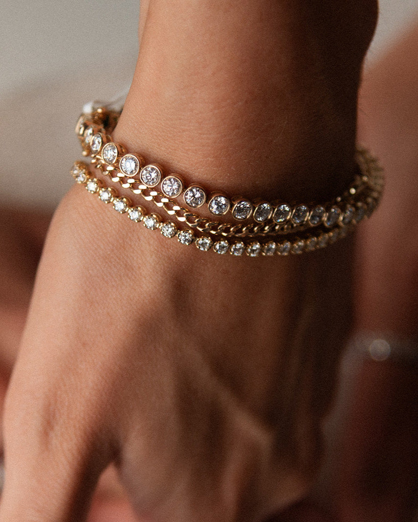 Close-up of a hand wearing multiple gold and diamond bracelets on a blurred background