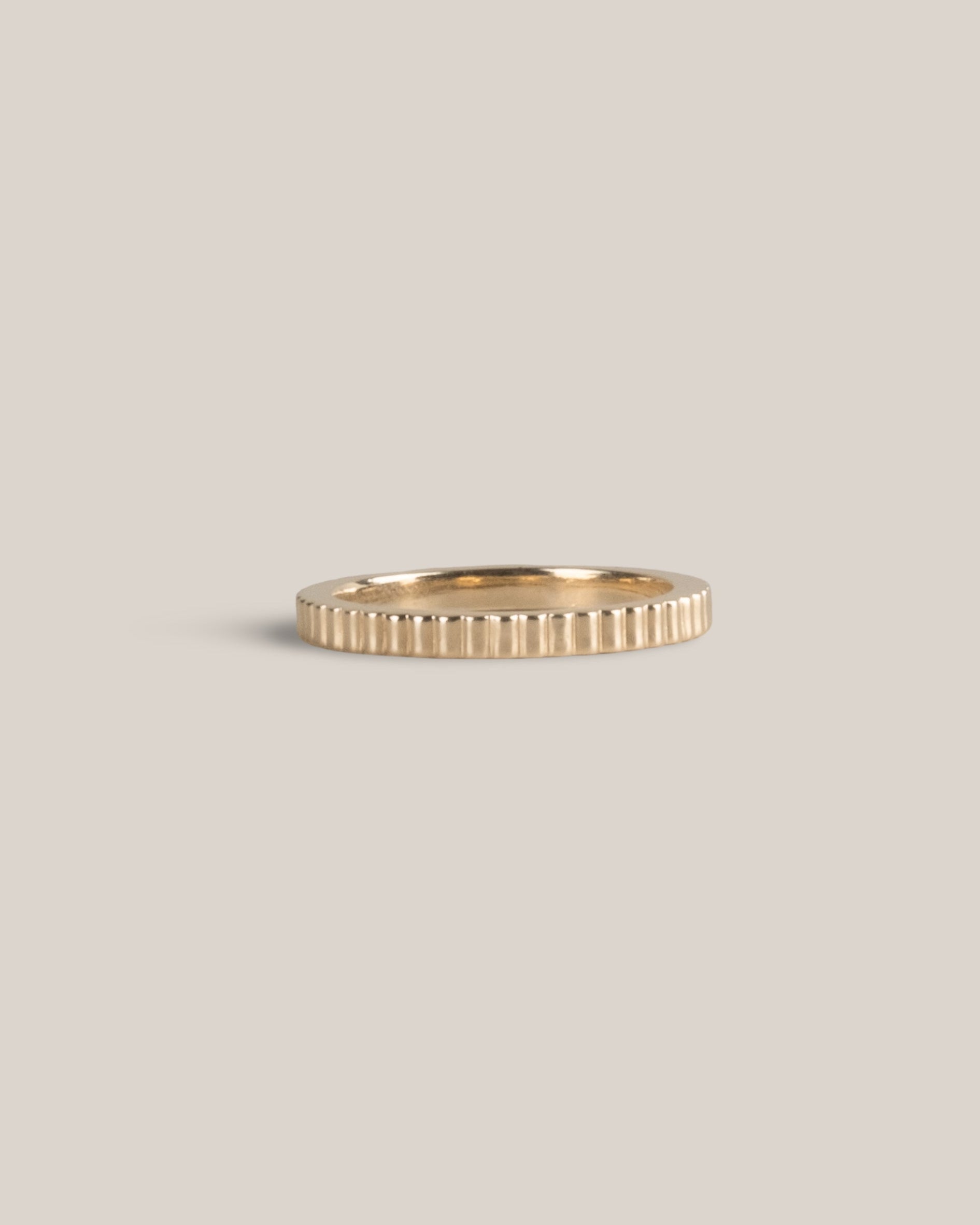 Gold ring with a textured band on a light beige background